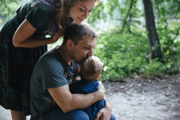 Счастливый молодой семьи отец, мать и маленький сын обнимаются и целуются на открытом воздухе, играть вместе в летнем парке Стоковое Изображение