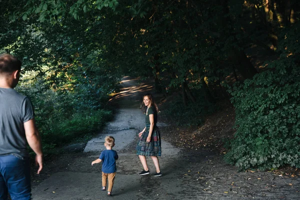 Счастливая молодая семья отец, мать и маленький сын обнимаются и трогают на улице, играя вместе в летнем парке Стоковое Изображение