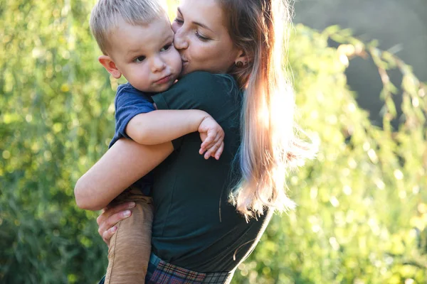 Front view mother and baby son hugging on the road on lake in summer evening time on the shurb background — Stock Photo, Image