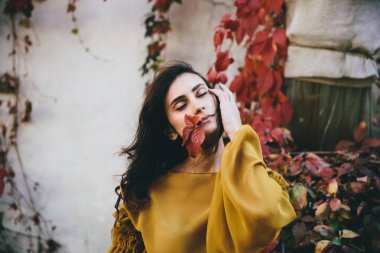 Sonbahar sokağında renkli yaprakları olan genç bir kadın. Turuncu yapraklar düşmüş ve etrafa dağılmış. Güneşli bir gün.