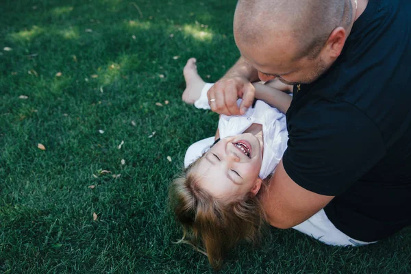 Schöne kleine blonde Mädchen hat fröhlichen Spaß lächelndes Gesicht spielt in einem weißen Kleid mit ihrem Vater, Kind und Vater Porträt. Kinderfamilie — Stockfoto