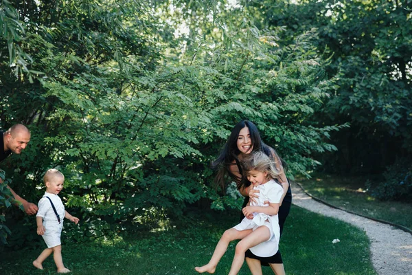 Familj av bror och syster i vita kläder leka med en pappa och mamma i parken eller trädgården — Stockfoto