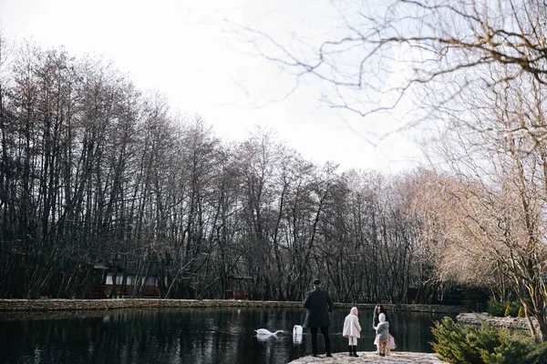 Gelukkig mooie familie voeding zwanen en wandelen door het meer op de herfst dag. — Stockfoto