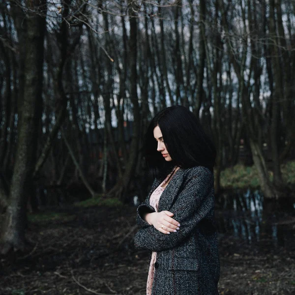 Giovane ragazza in un cappotto grigio scuro in piedi vicino al lago — Foto Stock