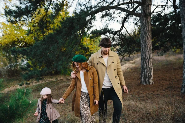 Genç Baba, anne ve bir Beret küçük yürümeye başlayan kız kızı ve sonbahar ormanında eller tutan bir ceket yürüyüş.