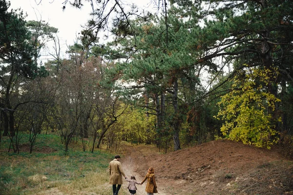 Junger Vater, Mutter und kleine Tochter in Baskenmütze und Mantel, Händchen haltend im herbstlichen Wald. zurück — Stockfoto