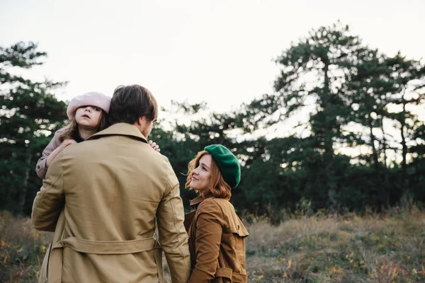 Junger Vater, Mutter und kleine Tochter in Baskenmütze und Mantelgang Händchen haltend im herbstlichen Wald. — Stockfoto