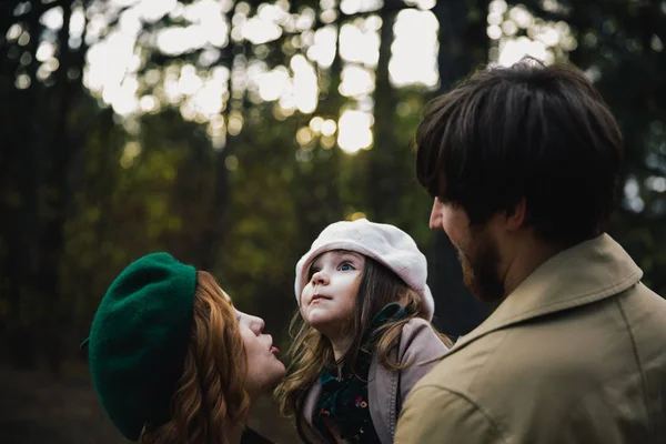 Joven padre, madre e hija pequeña en una boina y un paseo por el abrigo tomados de la mano en el bosque de otoño . —  Fotos de Stock