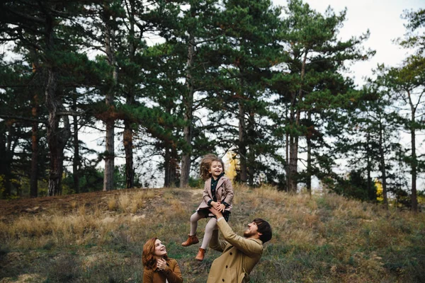 Young father, mother and little toddler daughter girl in a beret and a coat are having fun in the autumn forest. — Stock Photo, Image