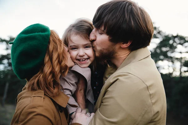 Jovem pai, mãe e pequena menina filha criança em uma boina e um casaco estão se divertindo e beijando um ao outro na floresta de outono . — Fotografia de Stock