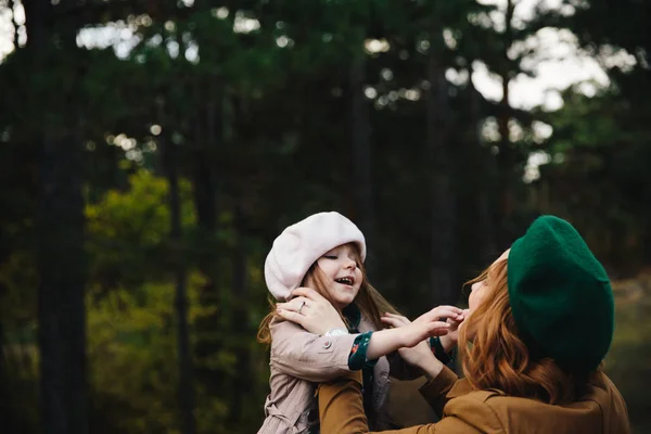 Joven madre e hija pequeña en una boina divirtiéndose entre sí en el bosque de otoño . —  Fotos de Stock