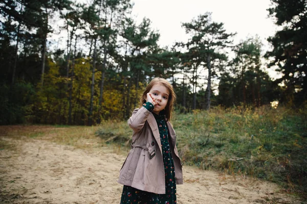 Красива дівчина в бежевому пальто лиже палець на сухій траві і осінньому лісовому фоні . — стокове фото