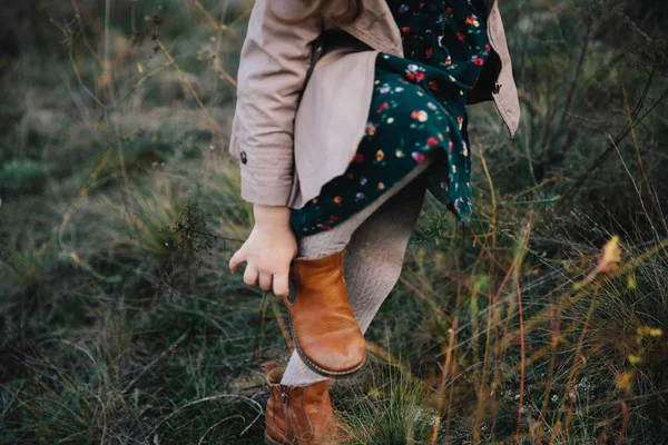 สาวผมสวยในรองเท้าโค้ทสีเบจ รองเท้ายางบนหญ้าแห้งและพื้นหลังต้นไม้ฤดูใบไม้ร่วง . — ภาพถ่ายสต็อก
