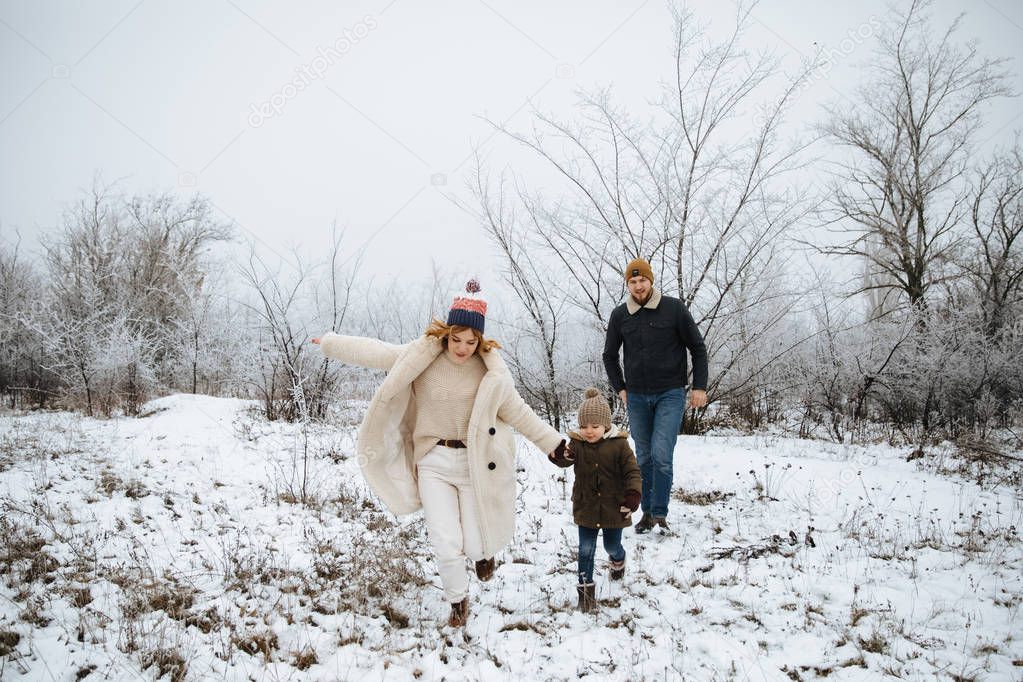 Happy family running on the snow field. Mom, dad, daughter stand outdoors on the background winter.