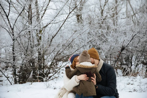 Happy family in coats and hats hugging on the snow field background. — Stock Photo, Image