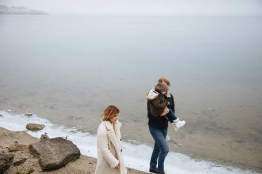 donmuş bir nehrin kıyısında yürüyen paltolu aile.