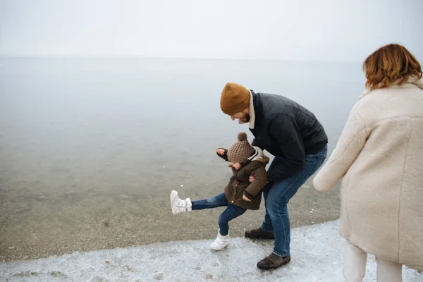 donmuş bir nehrin kıyısında yürüyen ve eğlenen paltolu aile.