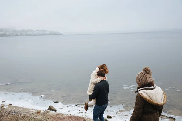 Familie in Mänteln spazieren und sich am Ufer eines zugefrorenen Flusses amüsieren. zurück — Stockfoto