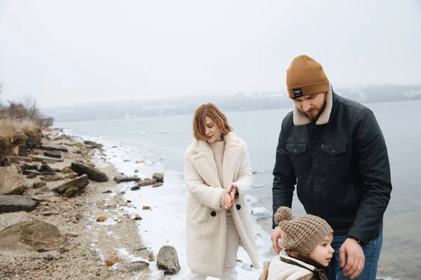 Familj i kappor gå och ha kul på stranden av en frusen flod. Back View — Stockfoto