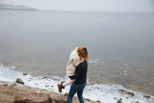 A couple in coats hugging on the banks of a frozen river — Stock Photo, Image