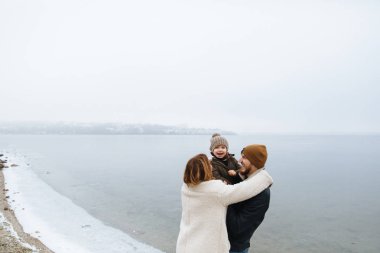donmuş bir nehrin kıyısında yürüyen paltolu aile.