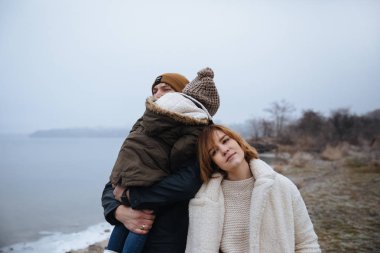 donmuş bir nehrin kıyısında sarılan ve poz veren paltolu aile.