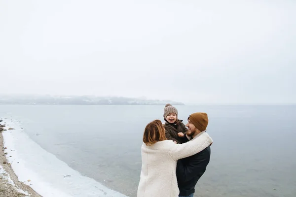 Familj i kappor gå på stranden av en frusen flod. — Stockfoto