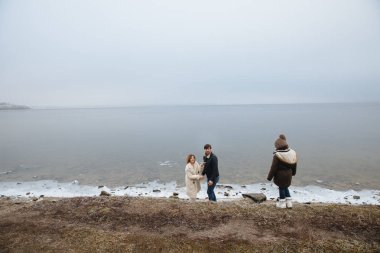 donmuş bir nehrin kıyısında yürüyen paltolu aile.