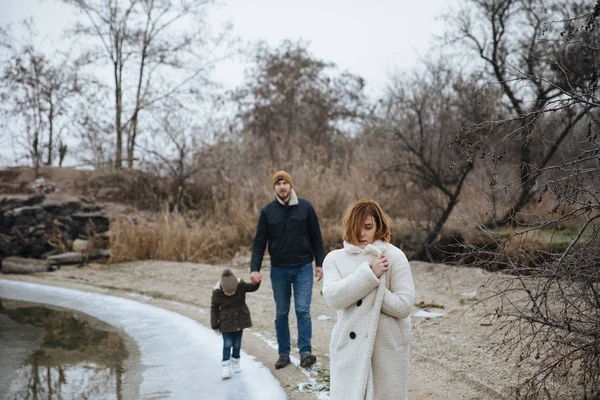 ครอบครัวในเสื้อโค้ท เดินบนฝั่งแม่น้ําแช่แข็ง . — ภาพถ่ายสต็อก