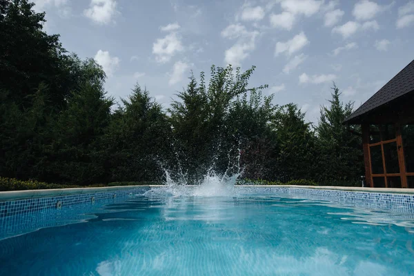 정원에서 수영장에서 점프 하는 젊은 남자. 건강한 라이프 스타일. 거대한 물 튀김 — 스톡 사진