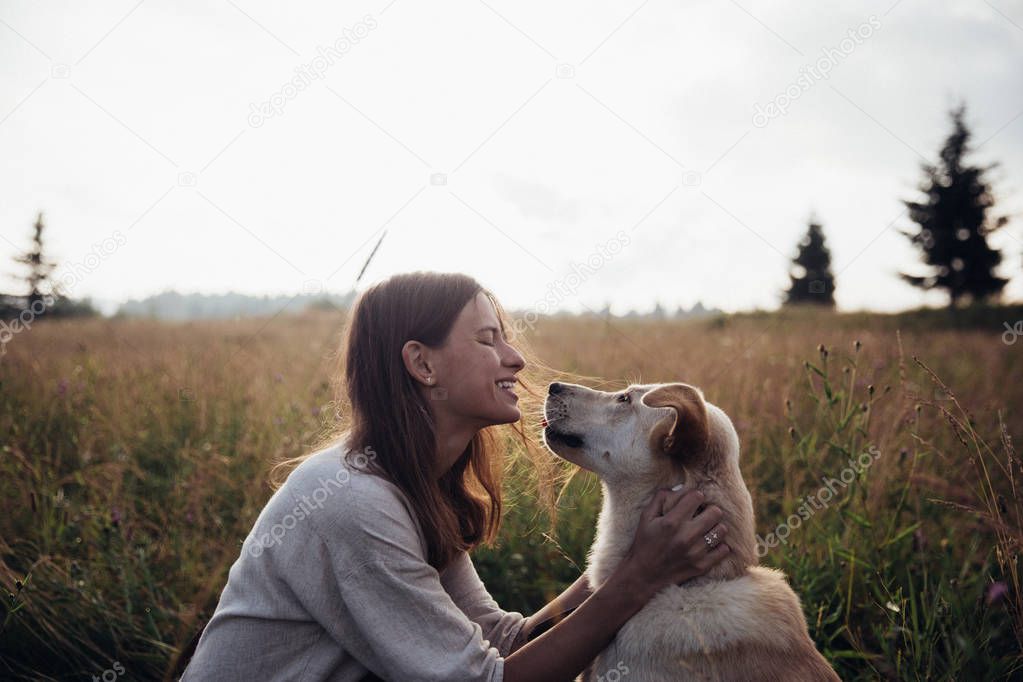 Beautiful young woman having fun summer sunset with her lovely dog on the straw field background
