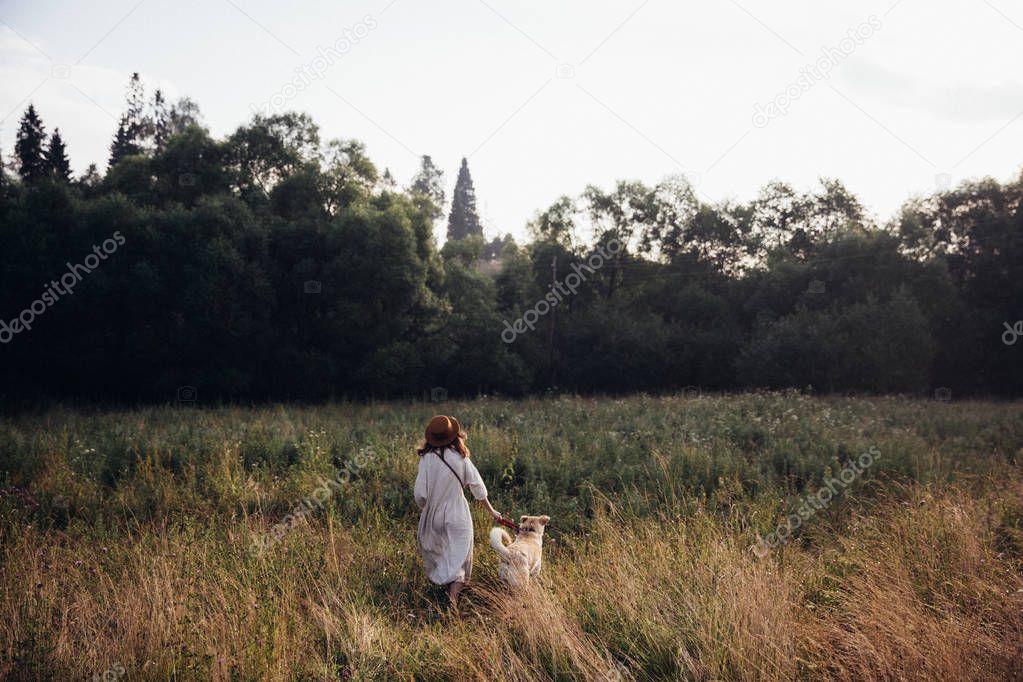 Beautiful young woman relaxed and carefree enjoying a summer sunset with her lovely dog on the straw field background. Back view