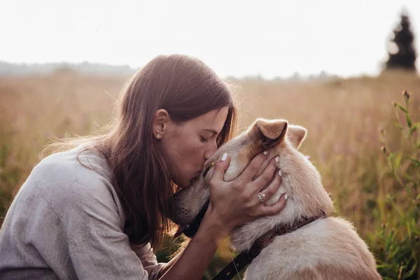 Humano y un perro. Chica y su amigo perro en el fondo del campo de paja. Hermosa joven mujer relajada y despreocupada disfrutando de una puesta de sol de verano con su adorable perro —  Fotos de Stock