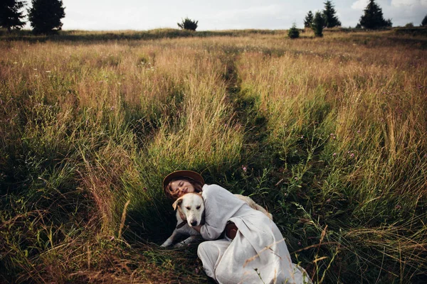เด็กผู้หญิงและสุนัขของเธอนอนอยู่บนพื้นหลังสนามหญ้า ผู้หญิงสาวที่สวยงามผ่อนคลายและไม่กังวลเพลิดเพลินกับพระอาทิตย์ตกฤดูร้อนกับสุนัขที่น่ารักของเธอ — ภาพถ่ายสต็อก