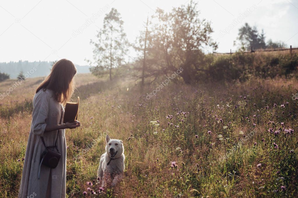 Girl and her dog are walking on the straw field background. Beautiful young woman relaxed and carefree enjoying a summer sunset with her lovely dog
