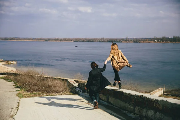 Junges Paar in warmen Mänteln amüsiert sich am Flussufer. — Stockfoto
