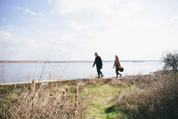 Young couple in warm coats having fun on the river bank. — Stock Photo, Image