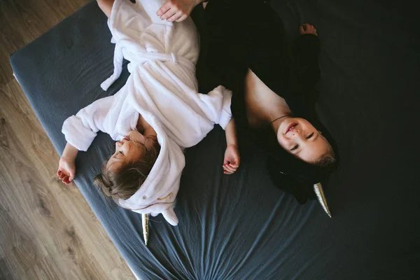 รูปภาพของเด็กสาวและเด็กชายที่ยิ้มน่ารักในชุดยูนิคอร์น นอนบนเตียงในร่ม — ภาพถ่ายสต็อก
