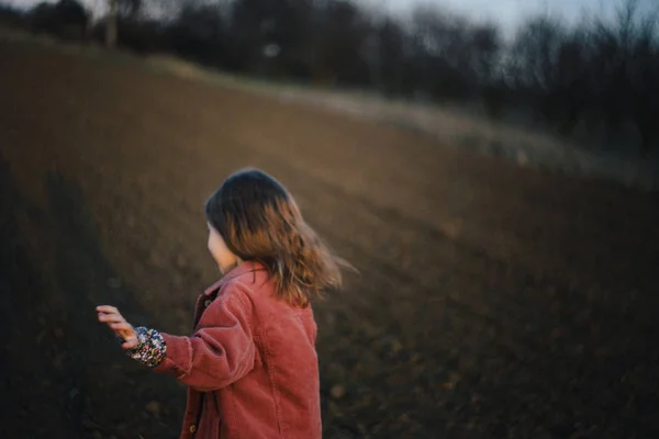 Rückansicht eines Mädchens im Herbstmantel, das bei Sonnenuntergang durch ein Weizenfeld geht. — Stockfoto