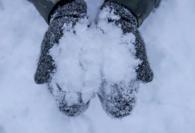 Kış arkaplanlı gri eldivenlerle karları elinde tutmaya yakın dur.
