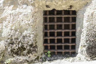 Paslı demir parmaklıklar, bir ortaçağ şatosunun içindeki kalın taştan bir duvara yerleştirilmiş. Demir parmaklıklı pencere ya da zindan ızgarası, Orta Çağ 'ın kale mimarisi ve savunma tarzını yansıtıyor.