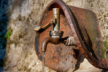 İsviçre 'nin Ticino kentindeki bir ormanda, taştan bir duvarda bulunan, sıcak güneş ışığıyla aydınlatılan, taştan bir metal borudan akan bir çeşme.