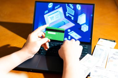 Masada USD banknotlarla online alışveriş yaparken kredi kartı tutan bir tüketicinin omuz üstü görüntüsü. Bir dijital çıkış işlemi sırasında nakit ve kart arasında satın alma kararı.
