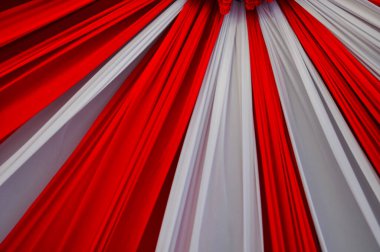 Kırmızı ve beyaz kumaş perdelerin radyal desende dizildiği güzel bir tavan dekorasyonunun detaylı bir görüntüsü. Ortadaki süs, canlı kırmızı ve beyaz çiçeklerle süslenmiş..