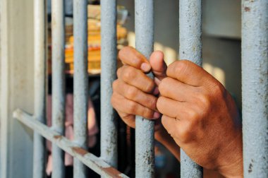  A Prisoner's Hands Reaching Out From Behind Metal Bars in a Jail Cell.