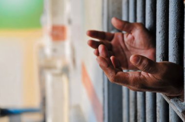  A Prisoner's Hands Reaching Out From Behind Metal Bars in a Jail Cell.