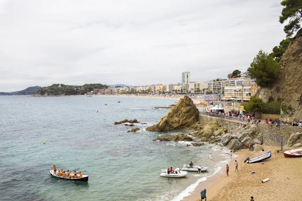 Bir Lloret de Mar / İspanya - 27 Haziran 2018: sahil Lloret de Mar, Costa Brava sahilden. İnsanlar Sahilde şezlong şemsiye altında yalan. Bir kale şehir sahilde altında istirahat.