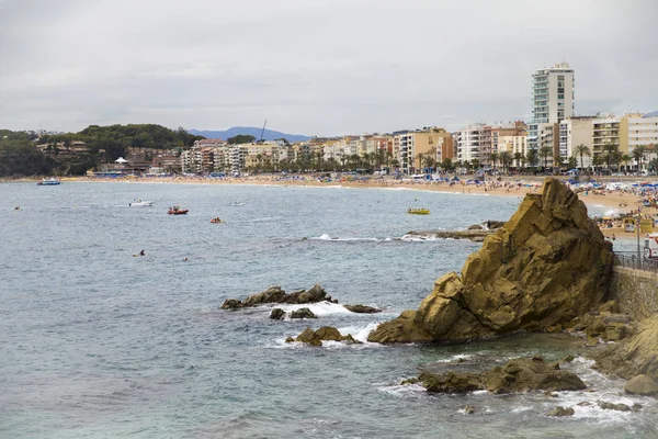 Bir Lloret de Mar / İspanya - 27 Haziran 2018: sahil Lloret de Mar, Costa Brava sahilden. İnsanlar Sahilde şezlong şemsiye altında yalan. Bir kale şehir sahilde altında istirahat.