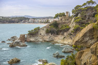 Bir Lloret de Mar / İspanya - 27 Haziran 2018: sahil Lloret de Mar, Costa Brava sahilden. İnsanlar Sahilde şezlong şemsiye altında yalan. Bir kale şehir sahilde altında istirahat.