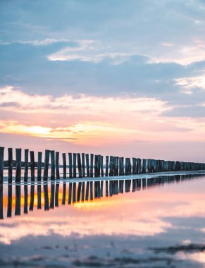 Lever du soleil et reflet dans l'eau de mer sur une plage en camargue avec des pcheurs au loin et des poteaux en bois
